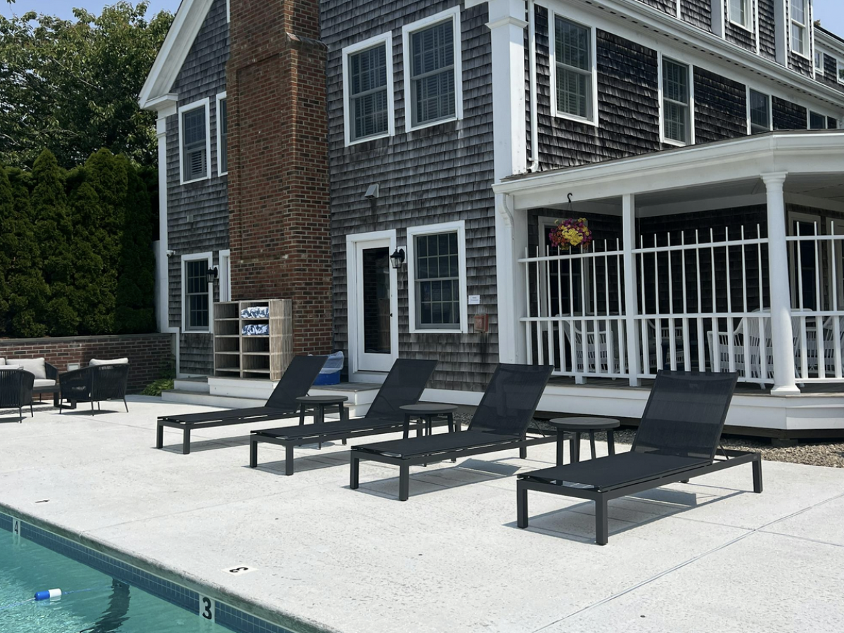 A modern house with a pool in the backyard, surrounded by lounge chairs and a patio area, featuring a large brick chimney and a wooden deck.