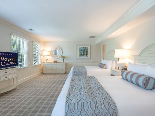 A spacious room features two double beds, a TV, a dresser with a mirror, and tasteful decor. A plaque reads "Chatham Wayside Inn."