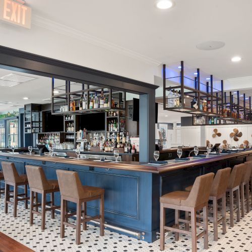 A modern bar setup with high chairs, a wide selection of bottles on the shelves, an overhead 