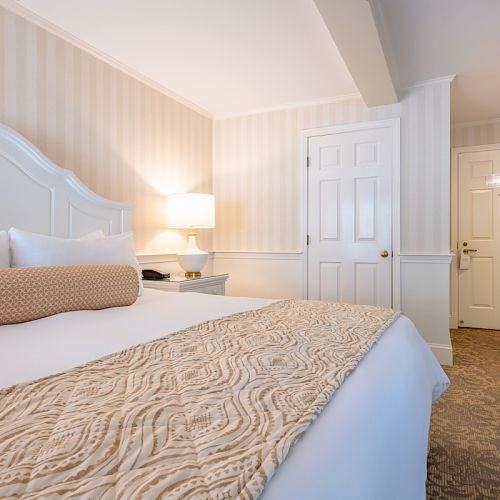 This image depicts a neatly arranged hotel room featuring a large bed with decorative pillows, a nightstand with a lamp, and a closed door.