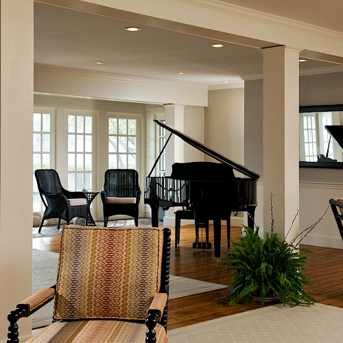 A spacious and elegant room with chairs, tables, a grand piano, potted plants, and large windows allowing natural light to fill the space, ending the sentence.