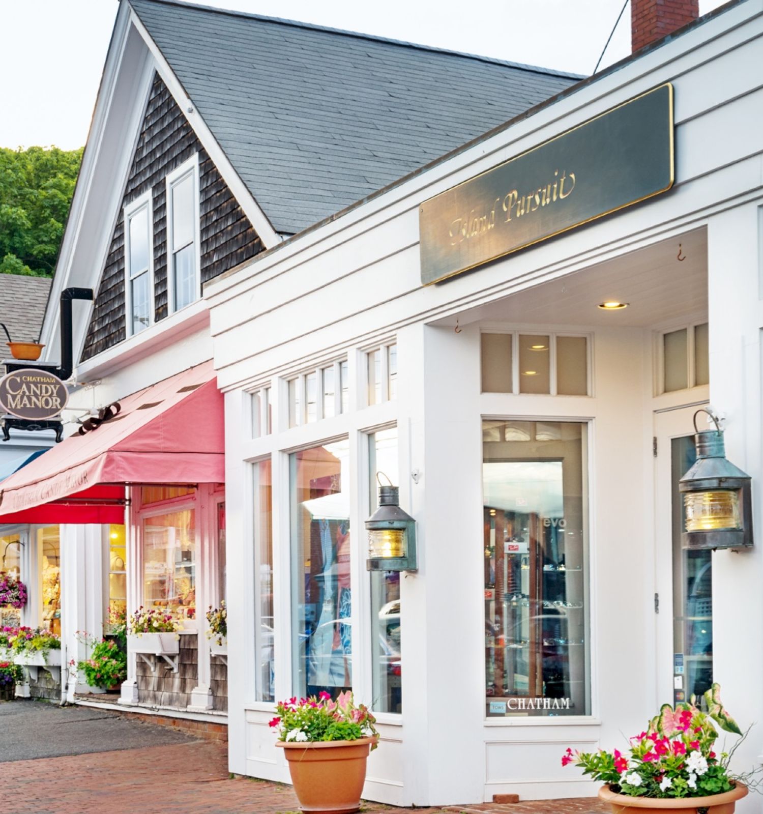 This image shows a charming street with various small shops, adorned with flower pots and brightly colored awnings, creating a quaint and inviting scene.