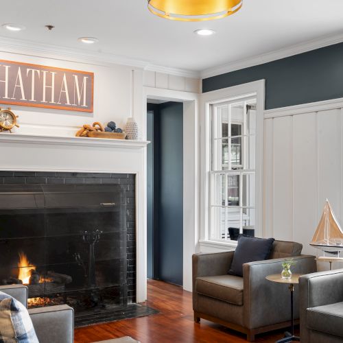 A cozy living room with a fireplace, comfortable seating, nautical decor, and a sign reading 