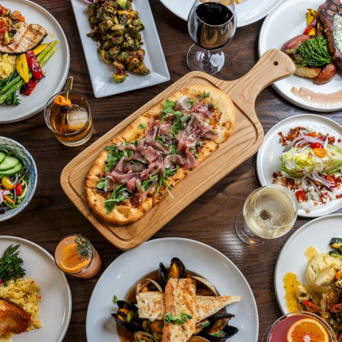 A spread of various dishes including grilled meats, pizza, salads, vegetables, and drinks on a wooden table.