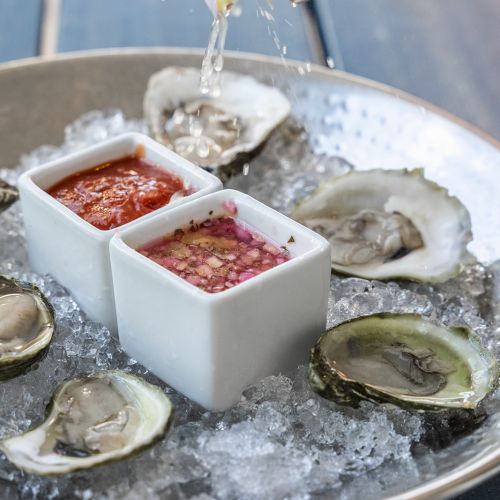 A platter of oysters on ice with dipping sauces and a hand squeezing lemon over the dish.