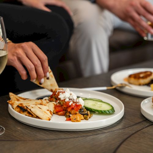 People are enjoying appetizers and drinks at a gathering, with three plates of food and a glass of wine visible on the table.