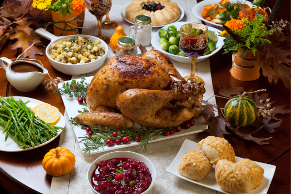 A Thanksgiving feast with turkey, stuffing, cranberry sauce, rolls, asparagus, Brussels sprouts, and pie, surrounded by autumn decor.