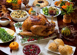 A Thanksgiving feast with roast turkey, cranberry sauce, stuffing, brussels sprouts, asparagus, bread rolls, and decorative pumpkins.