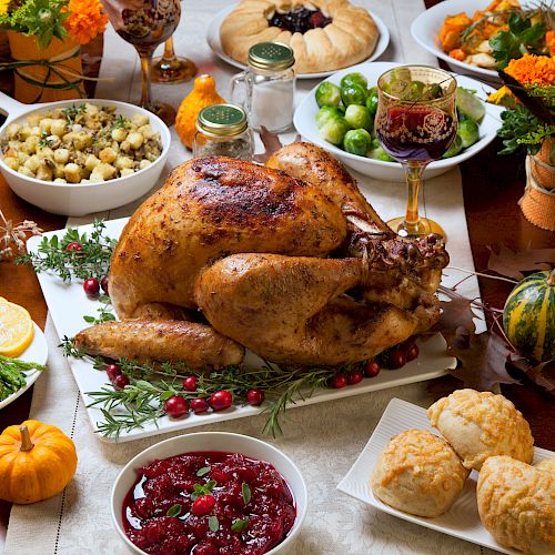 A Thanksgiving feast with roast turkey, cranberry sauce, stuffing, brussels sprouts, asparagus, bread rolls, and decorative pumpkins.