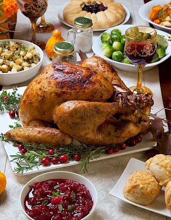 A Thanksgiving feast featuring a roast turkey, cranberries, stuffing, vegetables, rolls, and decorative pumpkins on a festive table.