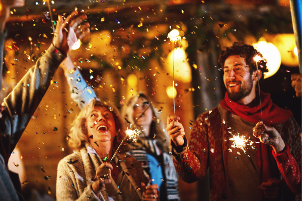 People are celebrating with sparklers, surrounded by festive lights and confetti, enjoying a joyful atmosphere.