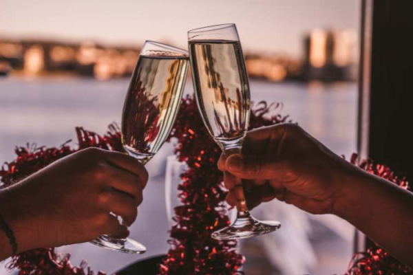 Two people clinking champagne glasses in celebration, with a blurred festive background and city skyline visible.