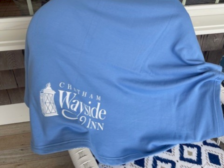 A chair is draped with a blue cloth that reads "Chatham Wayside Inn" next to a window.