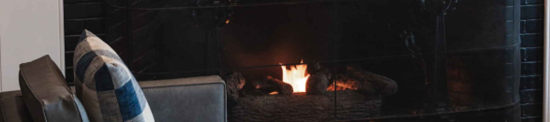 A cozy living room with a lit fireplace, chairs, and a "Chatham" sign above the mantel decorated with nautical items.