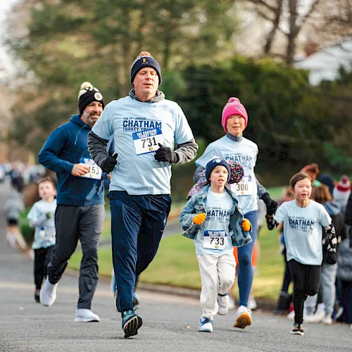 People run a &ldquo;Chatham Turkey Trot&rdquo; charity race, with kids in winter hats and bib numbers sprinting on a road outdoors.