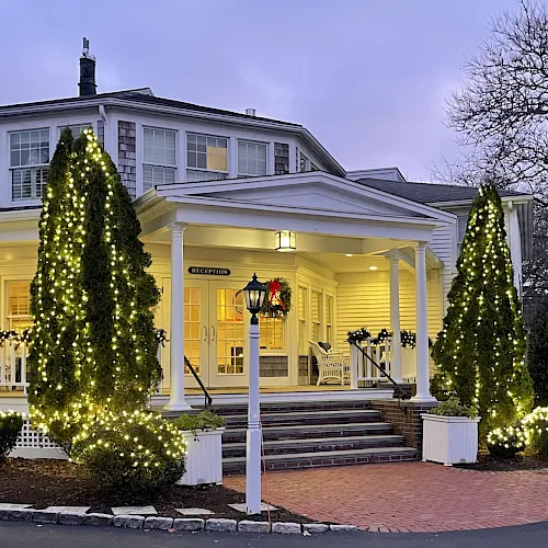 A hotel reception porch decorated for Christmas with lit conical trees, garlands, and warm evening lights.