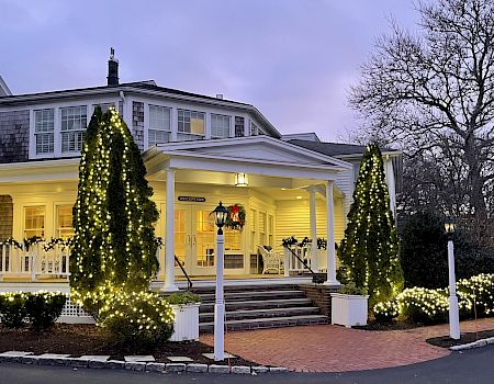 A hotel entrance at dusk, lit with glowing Christmas trees and warm lights, with a “RECEPTION” sign in the doorway.