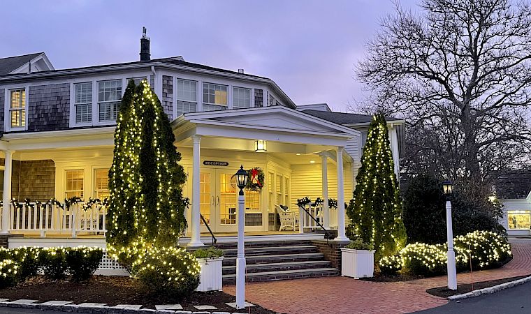 A hotel entrance at dusk, lit with glowing Christmas trees and warm lights, with a “RECEPTION” sign in the doorway.