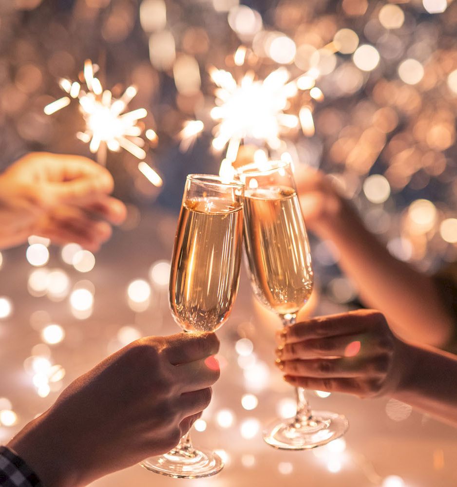 Two people clink champagne flutes while sparklers light up the celebration in the background.