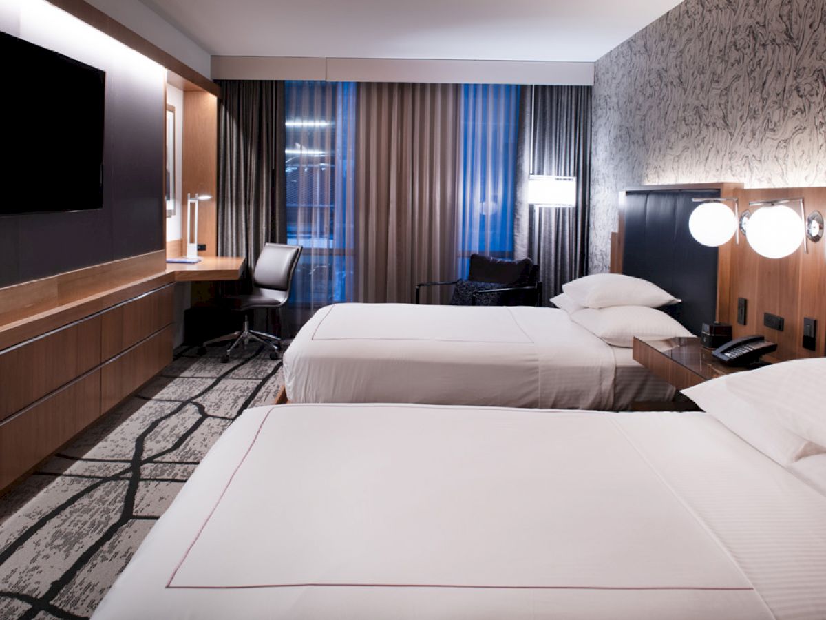 The image shows a modern hotel room with two neatly made beds, a flat-screen TV, a desk with a chair, and contemporary decor ending the sentence.